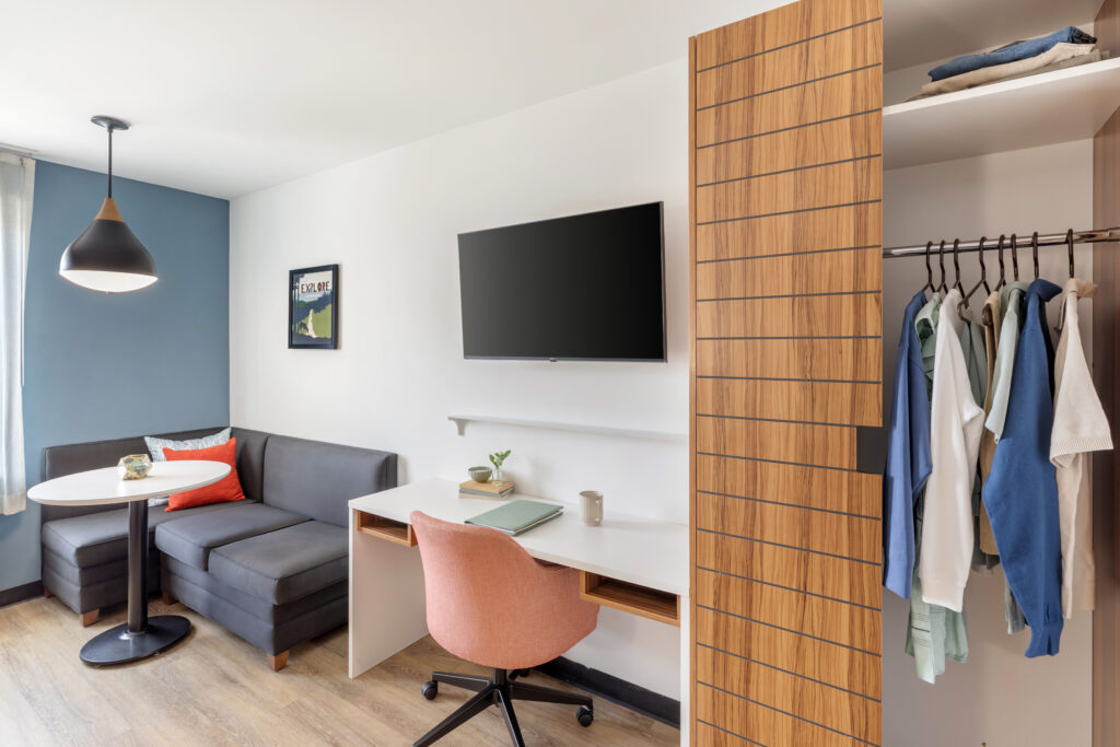 Desk area with wardrobe and sofa area and television.