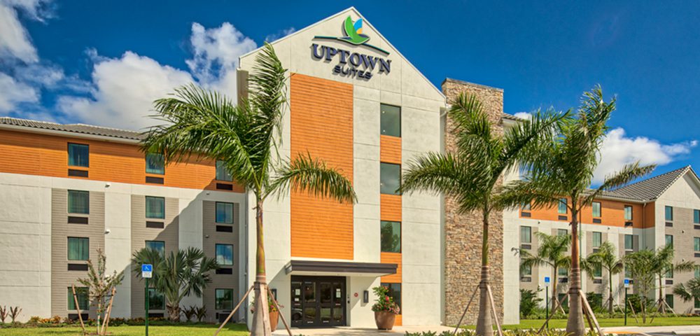 Exterior of Uptown Suites Extended Stay in Homestead, FL with two palm trees on the front and sunny sky 