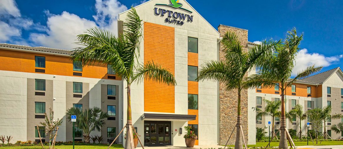 Exterior image of Uptown Suites property on sunny day with palm trees as landscaping