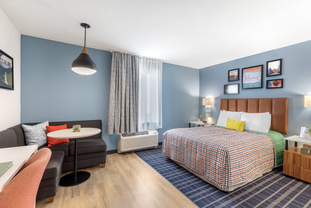 Full room view with single queen bed, corner sofa with table, large window and area for desktop working.