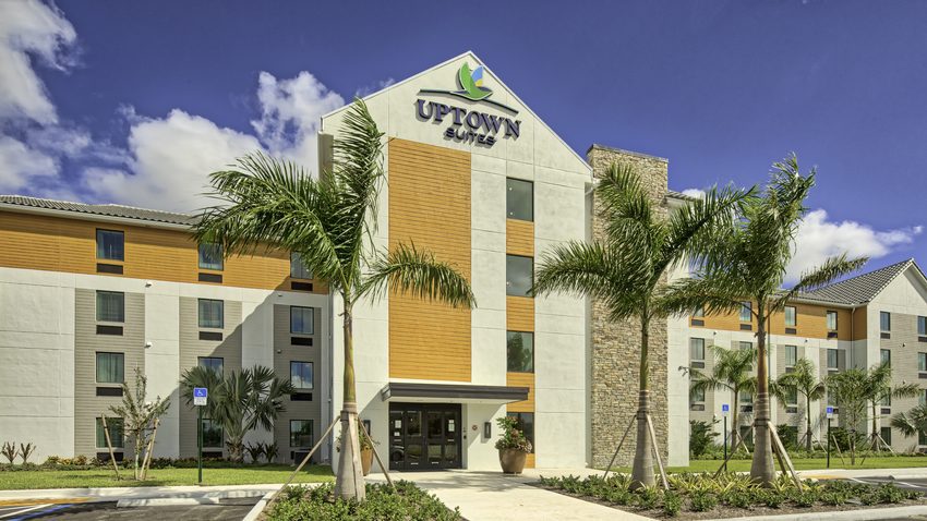 Exterior image of entrance to Uptown Suites on a sunny day, newly planted palm trees planted outside the lobby